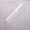 A white anti-static professional hair cutting comb lying on a cracked gray surface.