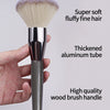 A close-up of a fluffy face powder brush with soft hair and a thickened aluminum tube, held in a hand.