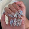 A hand displays 24 press-on fake nails with a light pink and white gradient finish and delicate pearl accents.