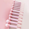 A collection of pink makeup brushes and puffs arranged in a vertical row on a light background.