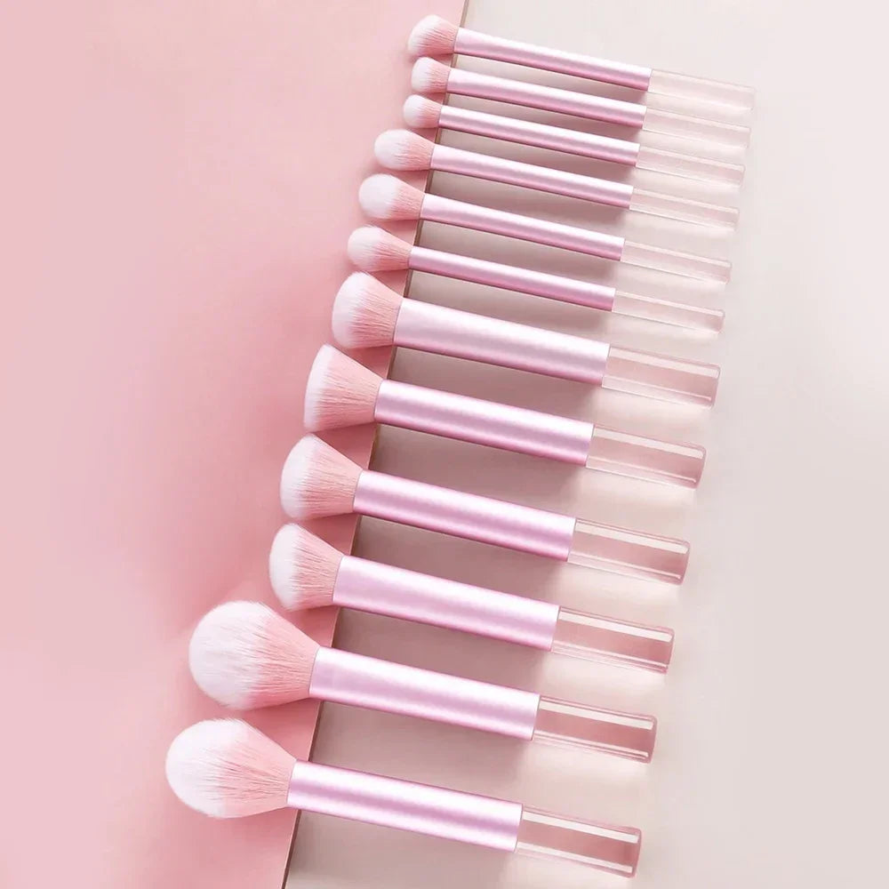 A collection of pink makeup brushes and puffs arranged in a vertical row on a light background.