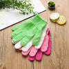 A stack of colorful exfoliating mitts in various shades of green, pink, and white are displayed on a wooden surface next to c