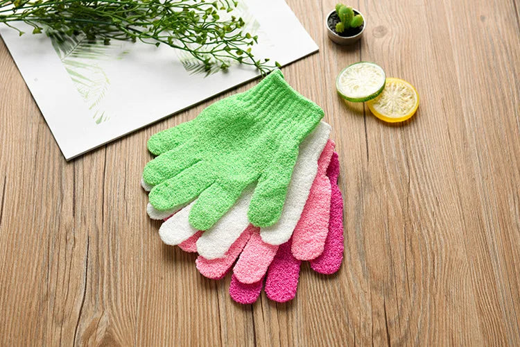 A stack of colorful exfoliating mitts in various shades of green, pink, and white are displayed on a wooden surface next to c