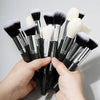 A hand holds a set of 30 professional makeup brushes with black and white bristles.
