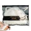 A black pouch containing a white African bath sponge is shown next to a person using the sponge in water.