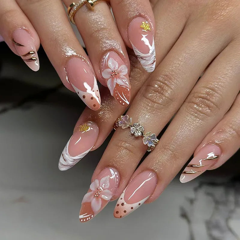 Close-up of manicured fingers displaying press-on false nails with a soft pink and white floral design and gold accents.