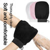 Black exfoliating body scrubbing gloves being worn on a hand, with other colored gloves visible in the background.