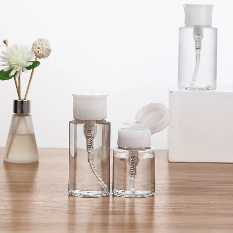 A set of clear glass refillable push-down pump dispenser bottles with white caps and a larger bottle in the background.
