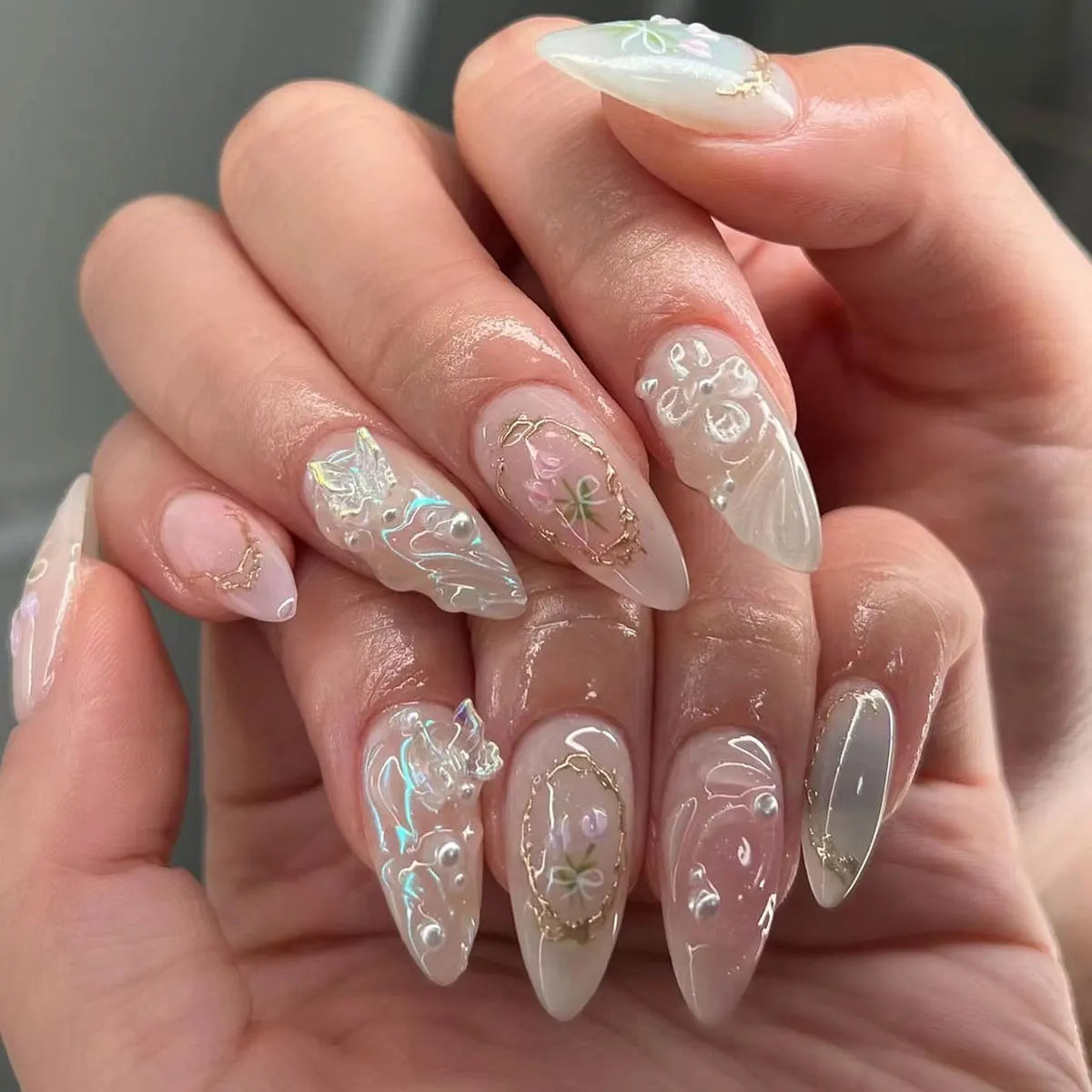 A hand displays a set of 24-piece almond press-on nails featuring delicate floral and butterfly designs.