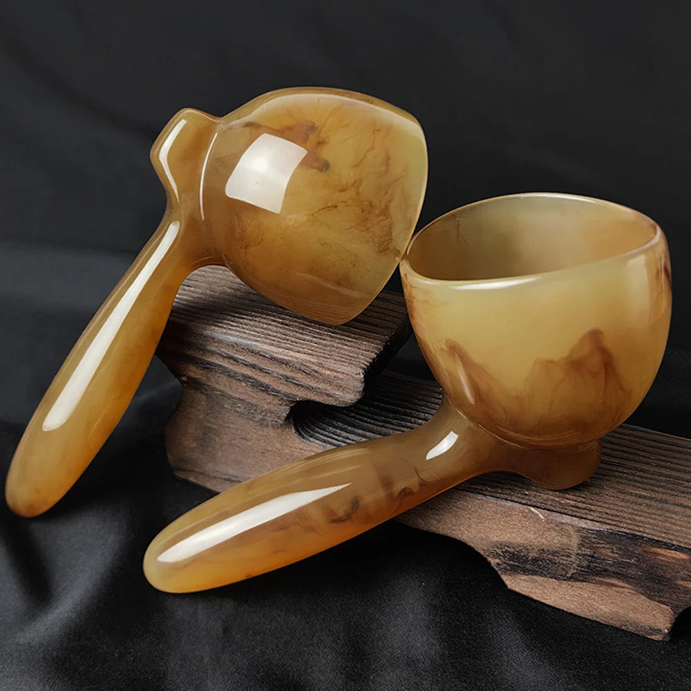 A smooth, amber-colored resin gua sha tool rests on a wooden surface.