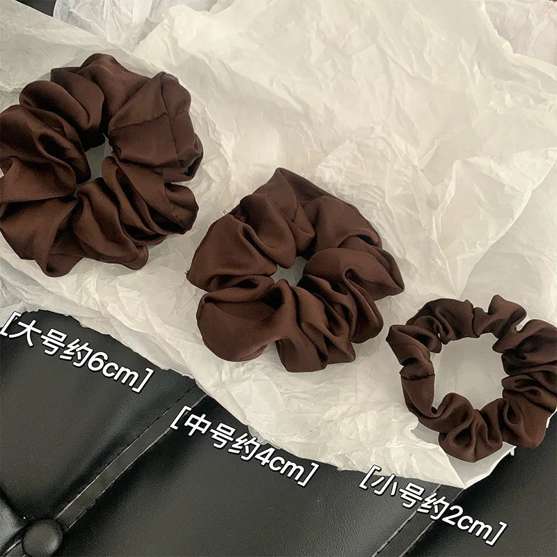 Collection de pinces à cheveux en satin de chiffon marron de différentes tailles, disposées sur du papier de soie blanc.