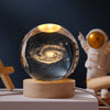 A glass crystal ball with a swirling galaxy design is displayed on a wooden base.