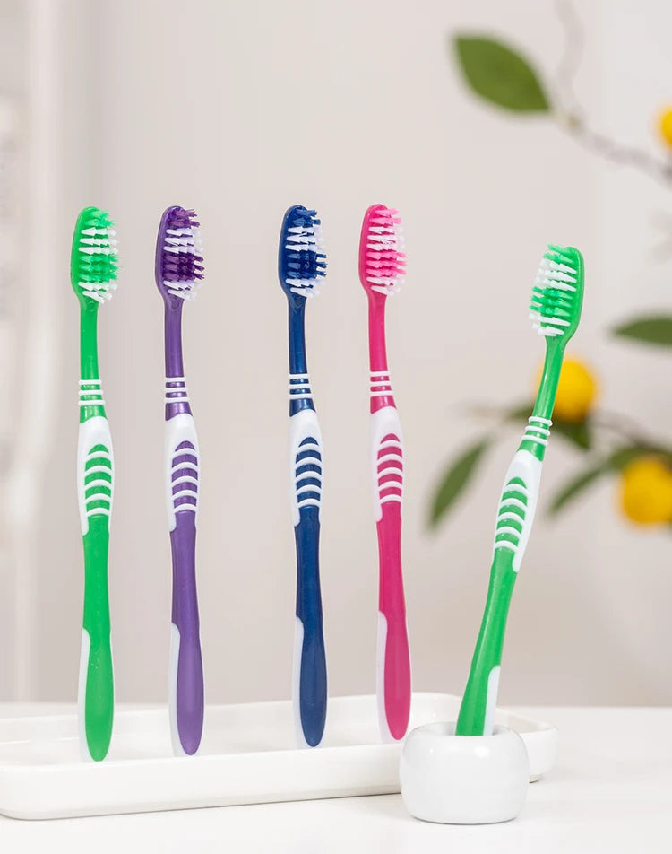 Une collection de brosses à dents manuelles colorées en vert, violet et rose sont présentées sur un plateau blanc.
