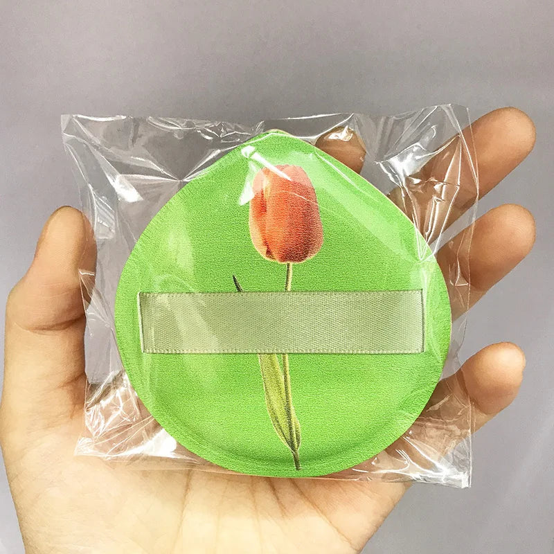 A green makeup puff with a dried orange rose on a white band is sealed in a clear plastic storage bag.