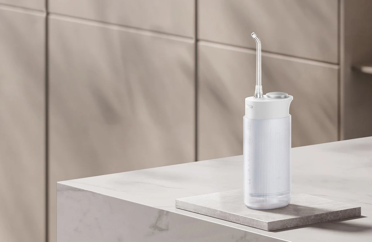 A white portable cordless oral irrigator with a clear nozzle is displayed on a light marble surface.