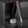 A professional hair dryer with a metallic finish is shown next to its detachable nozzle and drying components.