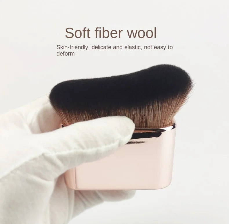 A hand holds a pink makeup brush with a black fiber bristles against a white background.