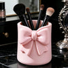 Organisateur de rangement rose contenant plusieurs pinceaux de maquillage sur une surface en marbre noir.