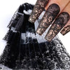Une main montre de longues ongles décorés de autocollants en dentelle noire sur un fond noir transparent.