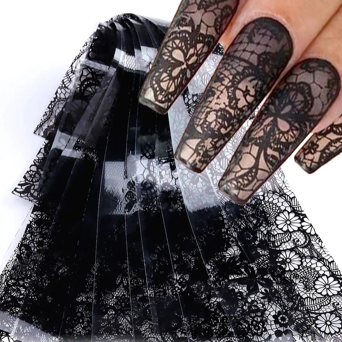 Une main montre de longues ongles décorés de autocollants en dentelle noire sur un fond noir transparent.