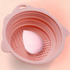 A pink silicone makeup brush cleaner and drying stand set with a perforated bowl holding a pink egg-shaped brush.