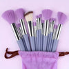 A set of purple and grey beauty sponges and brushes displayed on a pink background.