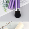 Un ensemble de pinceaux de maquillage rétractables violet et beige exposés sur une surface claire.