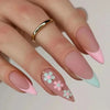 A hand displaying press-on false nails with a pink and green floral design and a gold ring.
