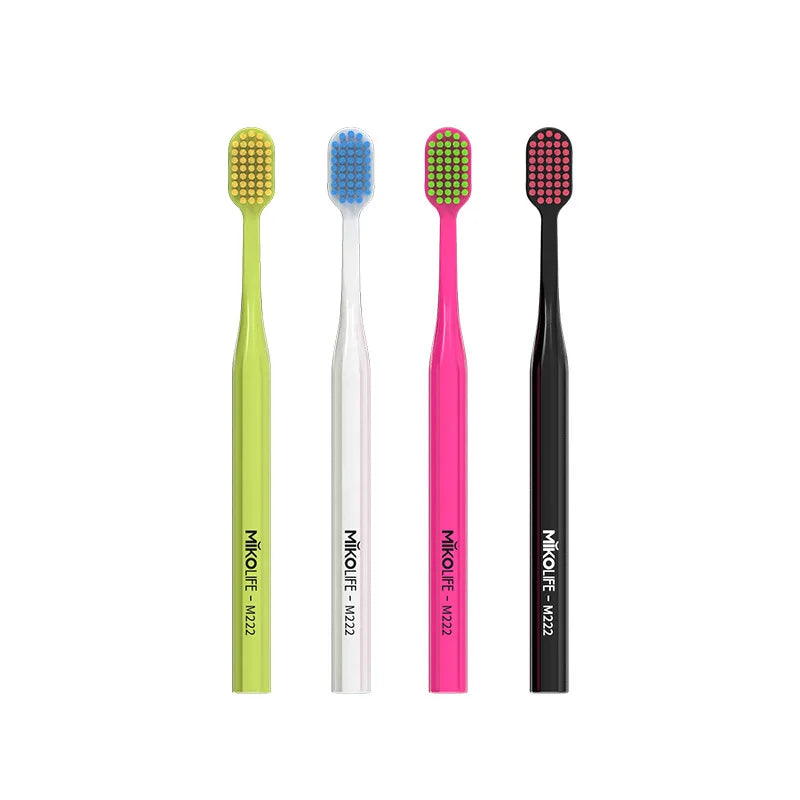 A set of four soft bristle manual toothbrushes in green, blue, pink, and black.