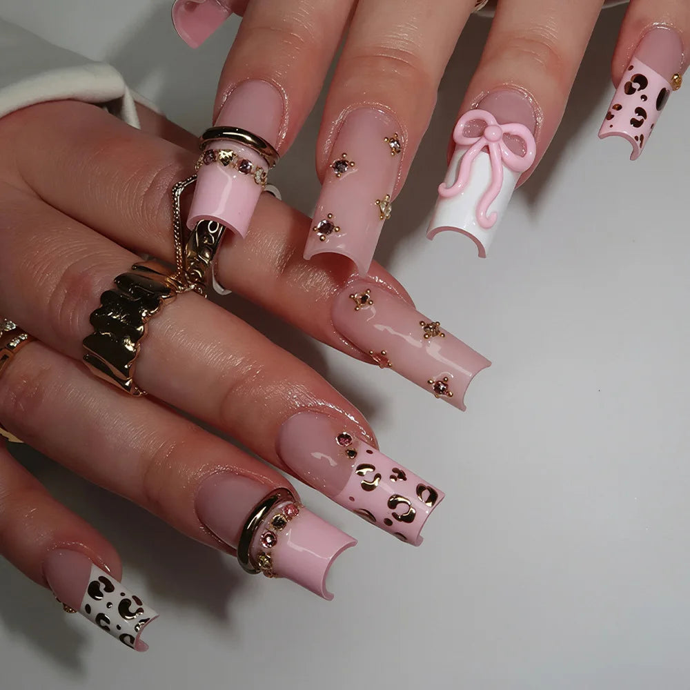A hand displaying gothic Y2K press-on nails featuring pink and black leopard print accents and delicate cross and bow designs