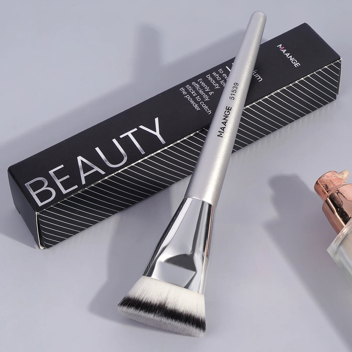 A silver Maange beauty flat kabuki foundation brush is shown next to its black packaging box.