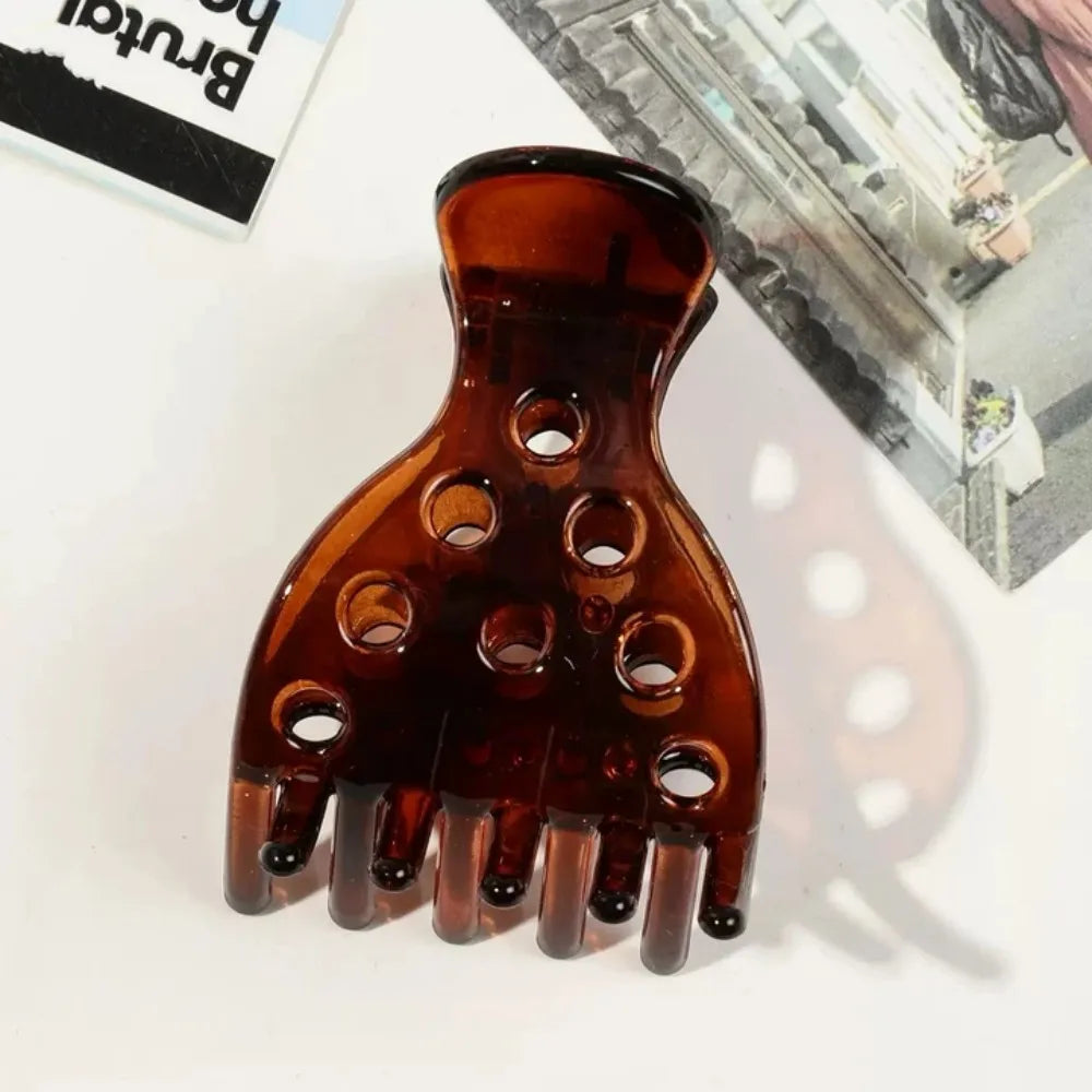 A close-up of a clear amber hair clip with multiple prongs used for root lifting and volume.