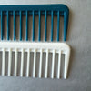 Two hair combs, one teal and one white, are displayed on a gray surface.