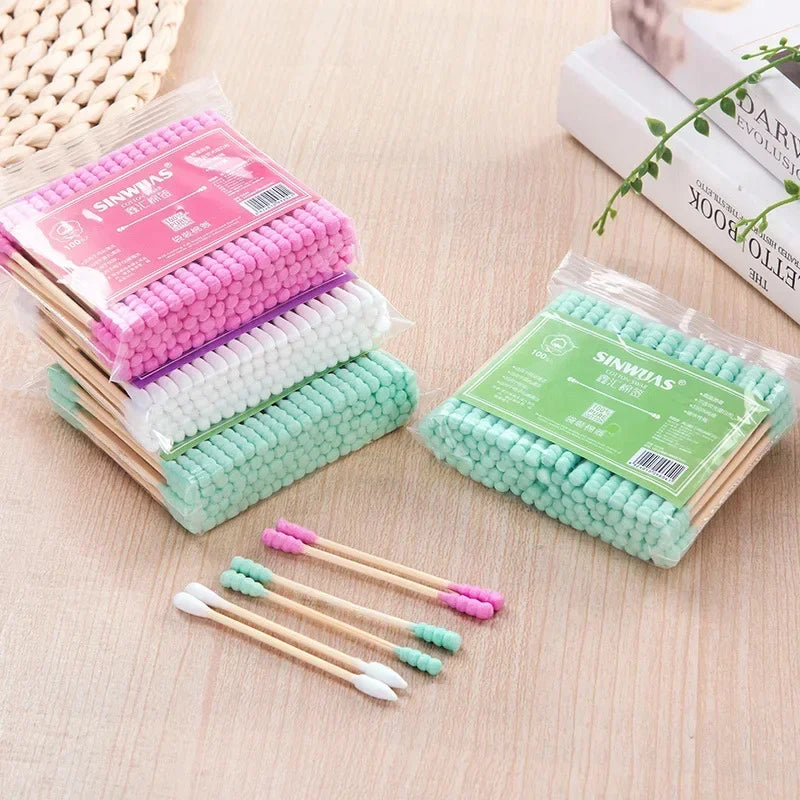 Collection de cotons-tiges en bambou rose et blanc emballés dans du plastique transparent, à côté d'un paquet vert similaire