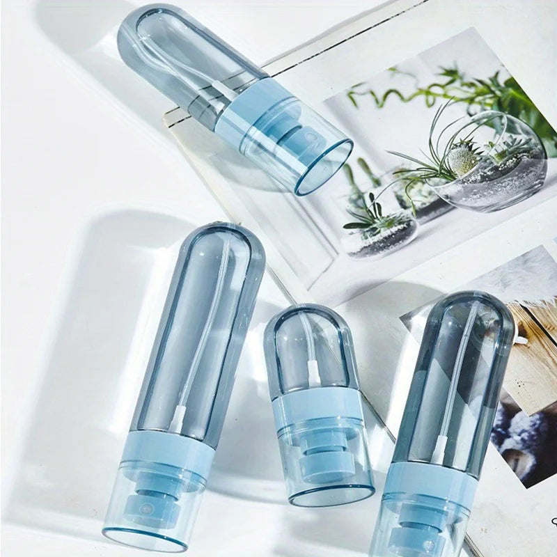 Clear blue portable refillable fine mist spray bottles displayed on a white surface with natural greenery.
