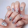 A hand displays various nail designs featuring iridescent and silver glass rhinestones for nail art.