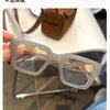 Une paire de lunettes de lecture carrées et transparentes avec des verres ambrés posées sur une surface.
