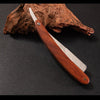 A professional wood handle shaving razor with a dark wooden handle and silver blade resting on a piece of bark.