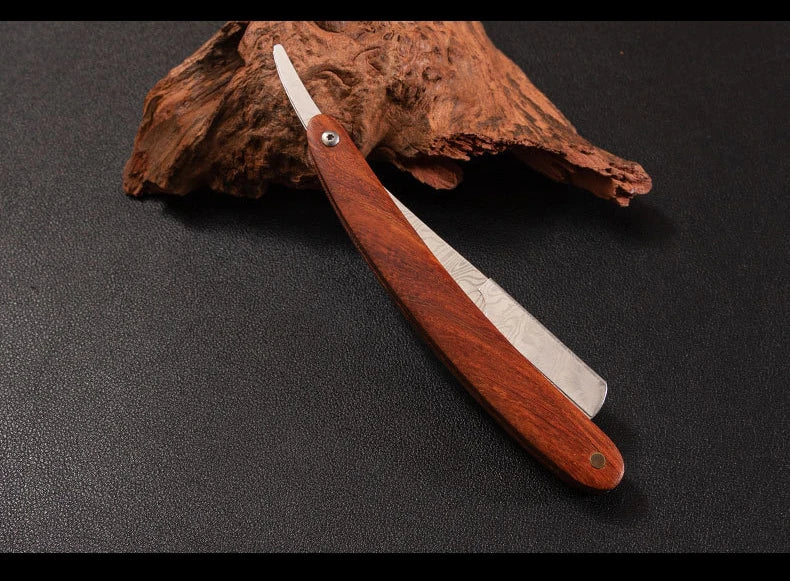 A professional wood handle shaving razor with a dark wooden handle and silver blade resting on a piece of bark.