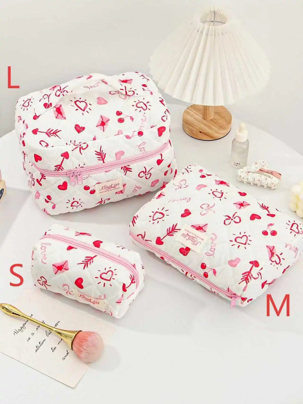Pink and white quilted cotton makeup bags in various sizes L, S, M, and M, with a lamp in the background.