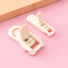 A pair of white cartoon mini eyelash curlers lying on a pink surface.