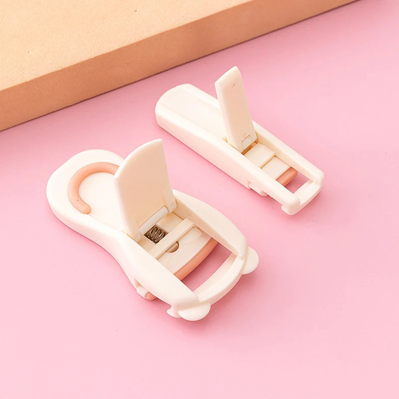 A pair of white cartoon mini eyelash curlers lying on a pink surface.
