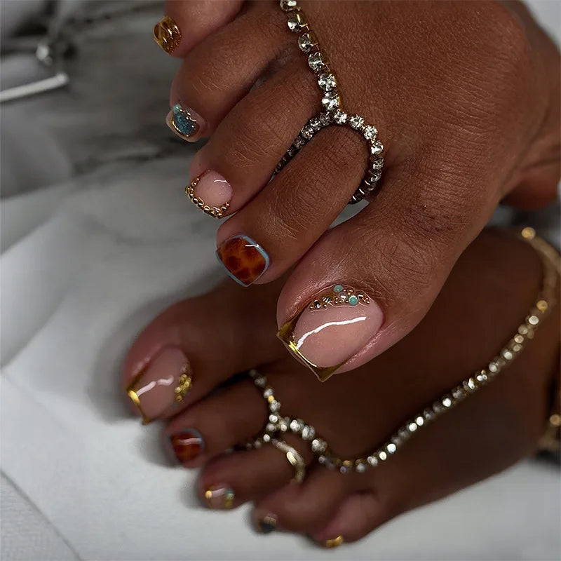 A hand displaying press-on fake nails with short square French design and gold accents.