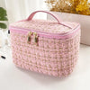 A pink knitted canvas makeup pouch with a pink lid and gold zippers resting on a white surface.