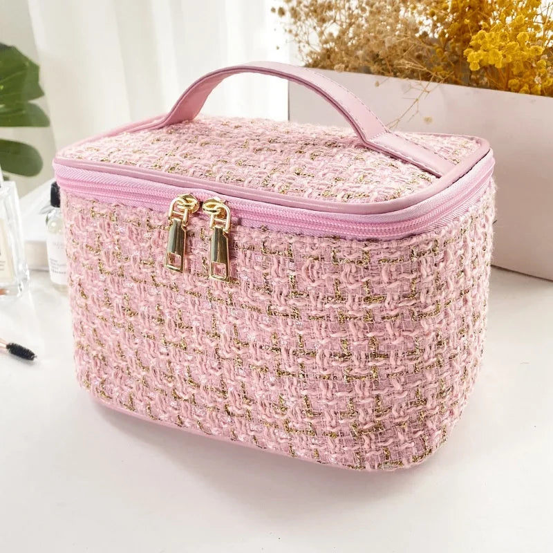 A pink knitted canvas makeup pouch with a pink lid and gold zippers resting on a white surface.
