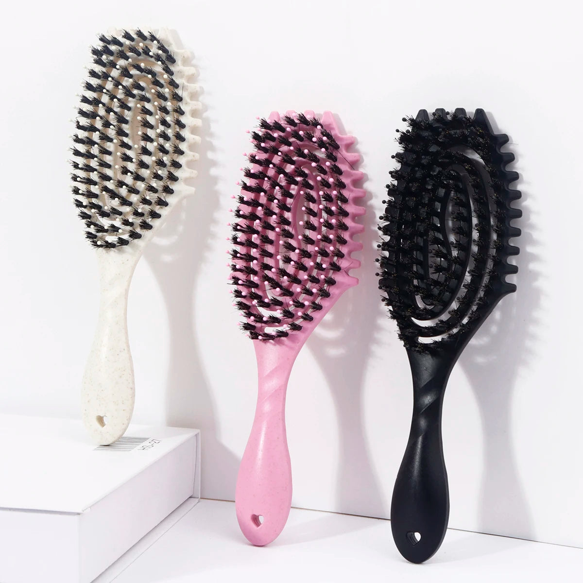 Three hair styling combs in black and pink bristles displayed on a white surface.