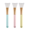 A set of three silicone facial mask applicator brushes in light blue, pink, and pale yellow.