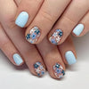 A close-up of a hand displaying press-on acrylic flower nails in light blue and white patterns.