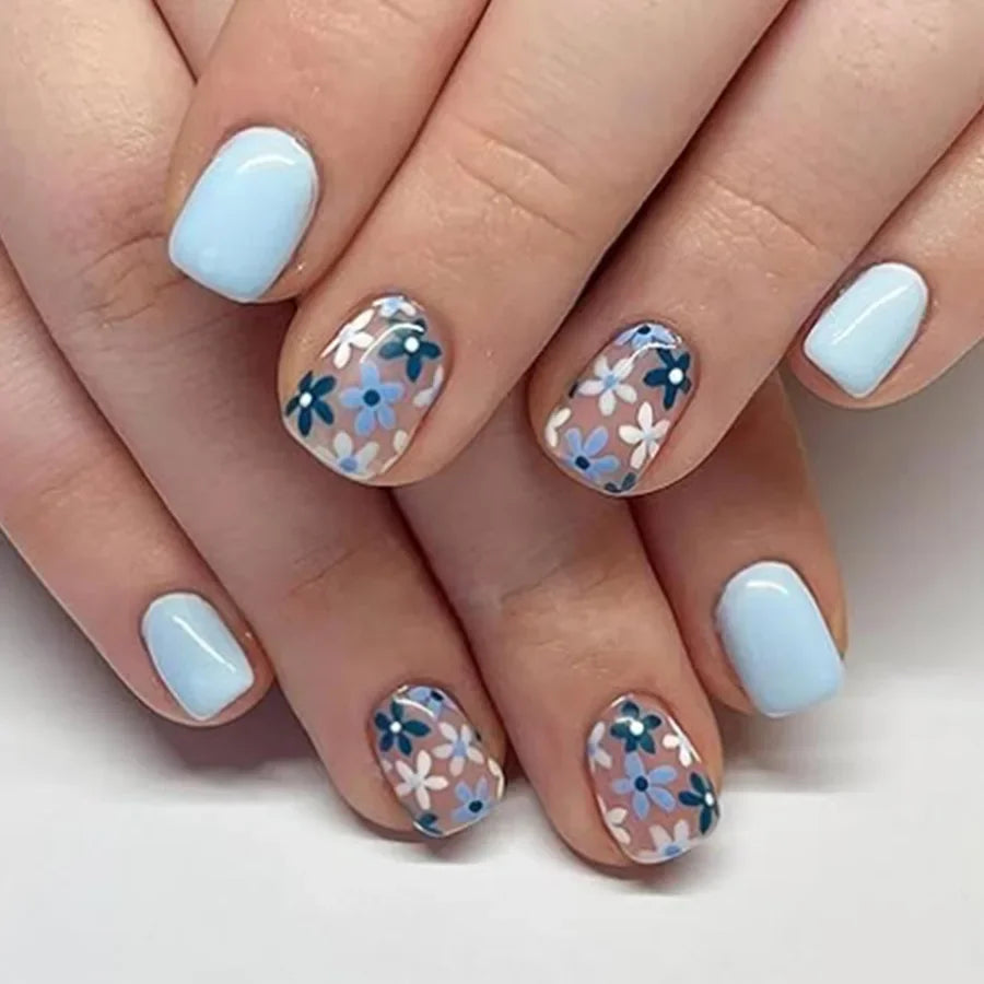 A close-up of a hand displaying press-on acrylic flower nails in light blue and white patterns.