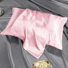 Pink satin heatless curling kit with silk accessories laid on a gray fabric background